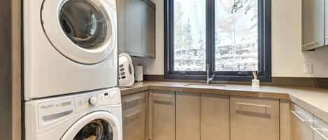 Una cocina moderna con lavadora doble, un amplio ventanal con vistas a árboles y armarios empotrados.