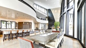 A spacious kitchen with a central island, a dining area with a large wooden table, and a modern staircase. - The Colony at White Pine Canyon by KBM (Park City)