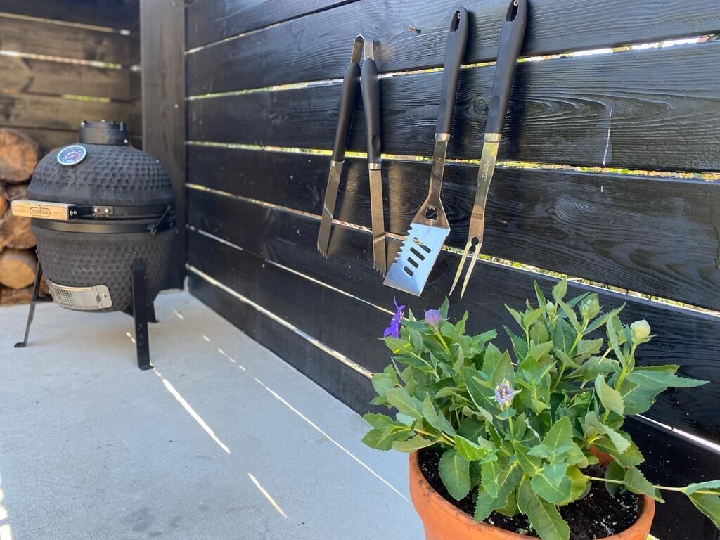 A barbecue grill, two barbecue tongs, and a potted plant on a patio.