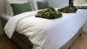 Una cama bien hecha con ropa de cama blanca y dos toallas verdes dobladas encima.