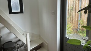Una habitación pequeña con una escalera de madera, un ventanal y una puerta que da al exterior.