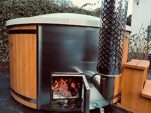 A wood-burning stove with a metal chimney, surrounded by wooden structures and greenery. - Ameland-style atmosphere with a wood-fired bath, 250 m from the center of Hollum (Hollum)