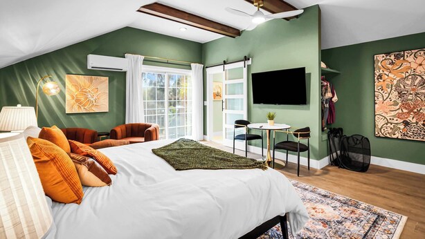 Een slaapkamer met een groot bed, een bureau, een stoel, een plafondventilator en een televisie aan de muur.
