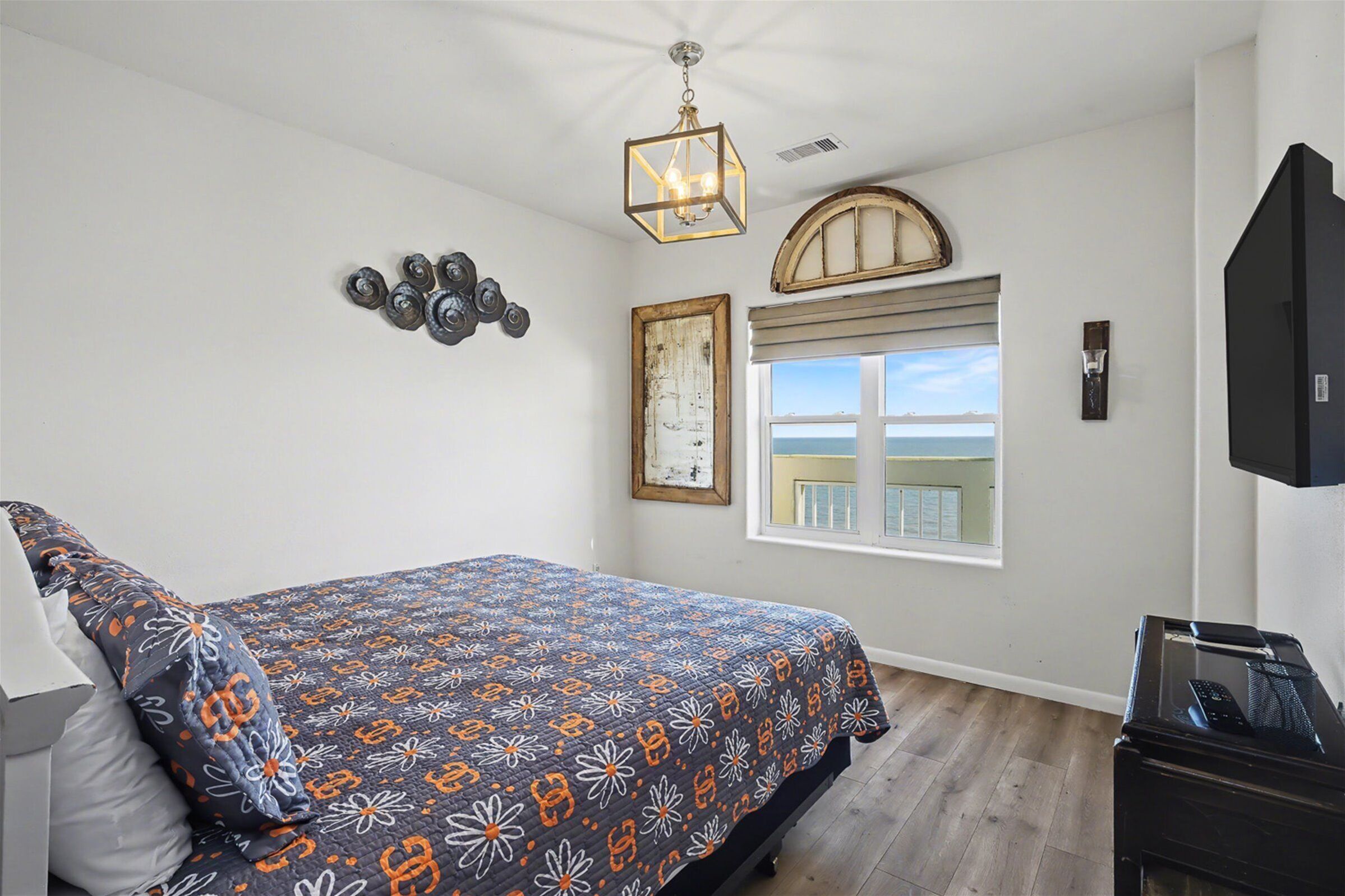 A bright bedroom with a patterned bed, geometric light, and a window facing the water.