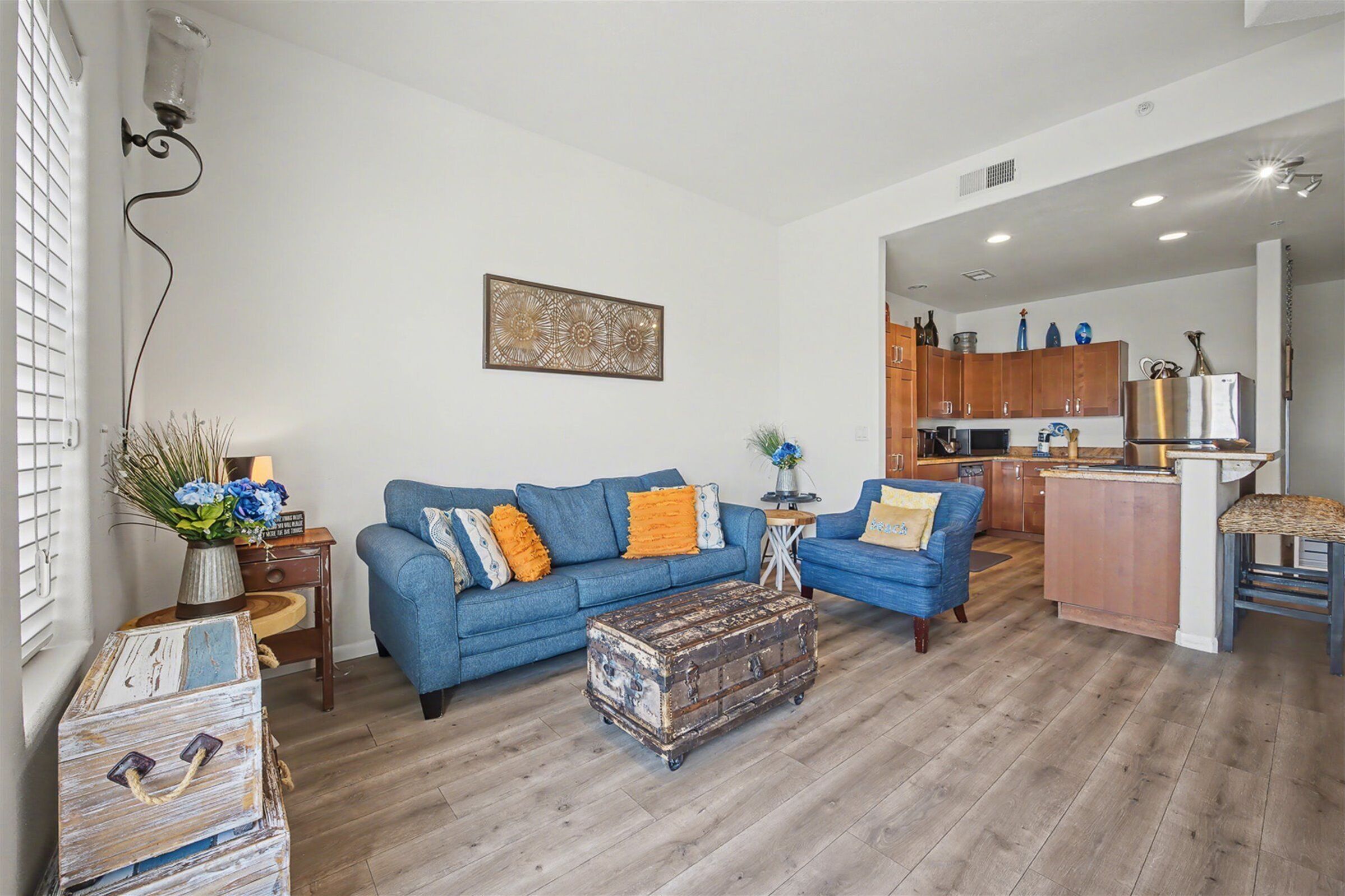 Ein Wohnzimmer mit einem blauen Sofa, einem Holztisch und einer Küche im Hintergrund.