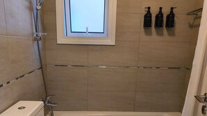 A bathroom with a bathtub, toilet, and a window. There are three bottles on the wall. - Casa Clara apartment with sea view on the beach (Chloraka)