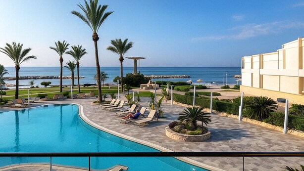 A swimming pool with lounge chairs and palm trees, overlooking a beach and ocean. - Casa Clara apartment with sea view on the beach (Chloraka)