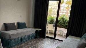 A hotel room with a large bed, a smaller bed, a desk, and a balcony with a view of buildings and greenery. - Casa Clara apartment with sea view on the beach (Chloraka)