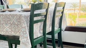 A dining table with chairs, a patterned tablecloth, and a view of palm trees through a window. - Casa Clara apartment with sea view on the beach (Chloraka)