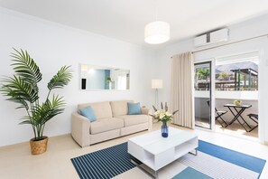 Un salon moderne avec un canapé, une table basse, une plante en pot, un miroir et une vue sur l’extérieur.