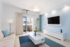 Un salon moderne avec un canapé, une table basse, un téléviseur et un balcon aménagé avec du mobilier d’extérieur.