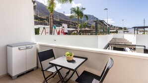 Un balcon avec une table et des chaises, un petit meuble et une vue sur un terrain de jeux et des montagnes.