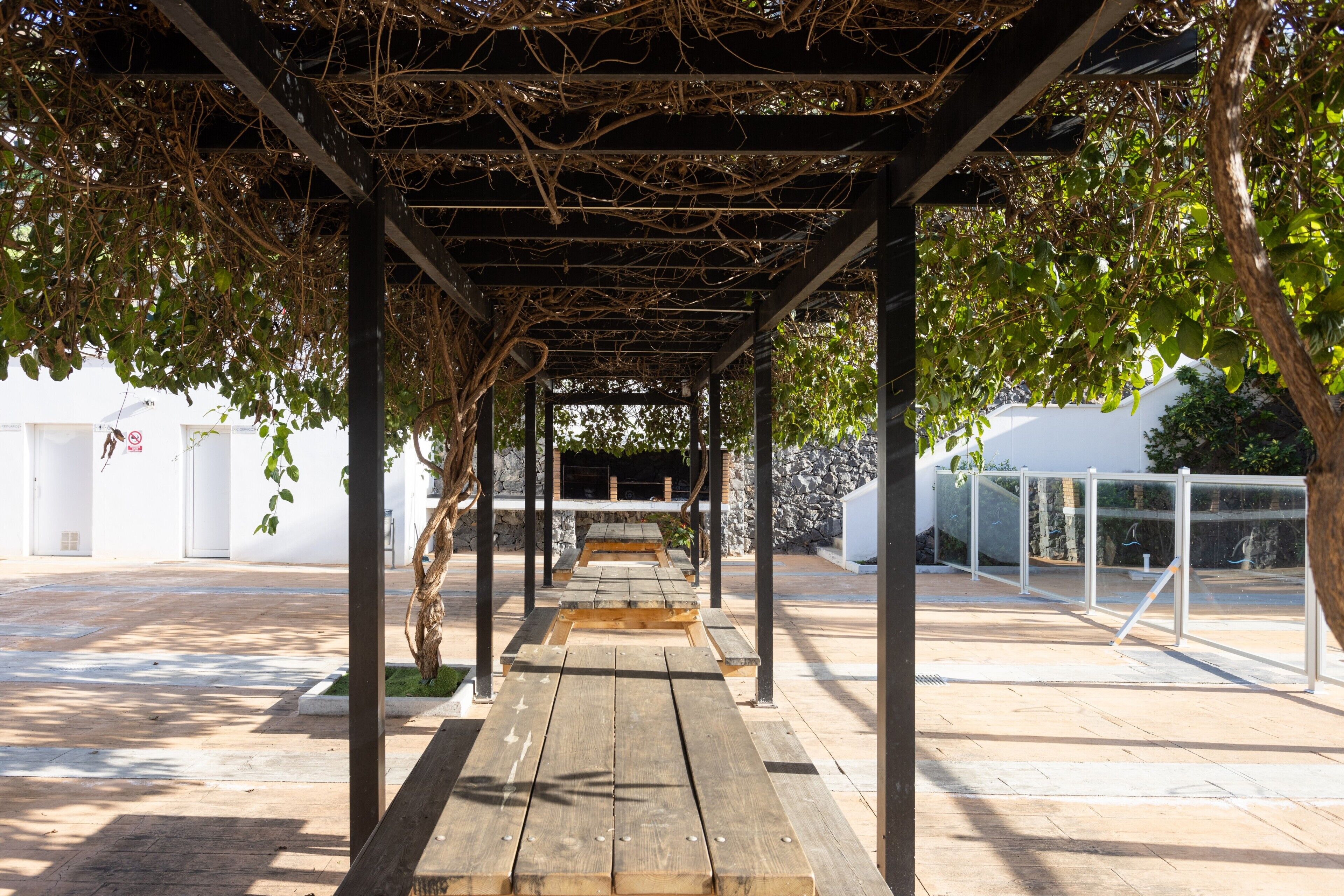 Un área de estar al aire libre techada, con bancos de madera y una estructura de pérgola.