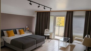 Una habitación de hotel con una cama, dos mesitas de noche, una silla, una pequeña mesa y una ventana con cortinas.