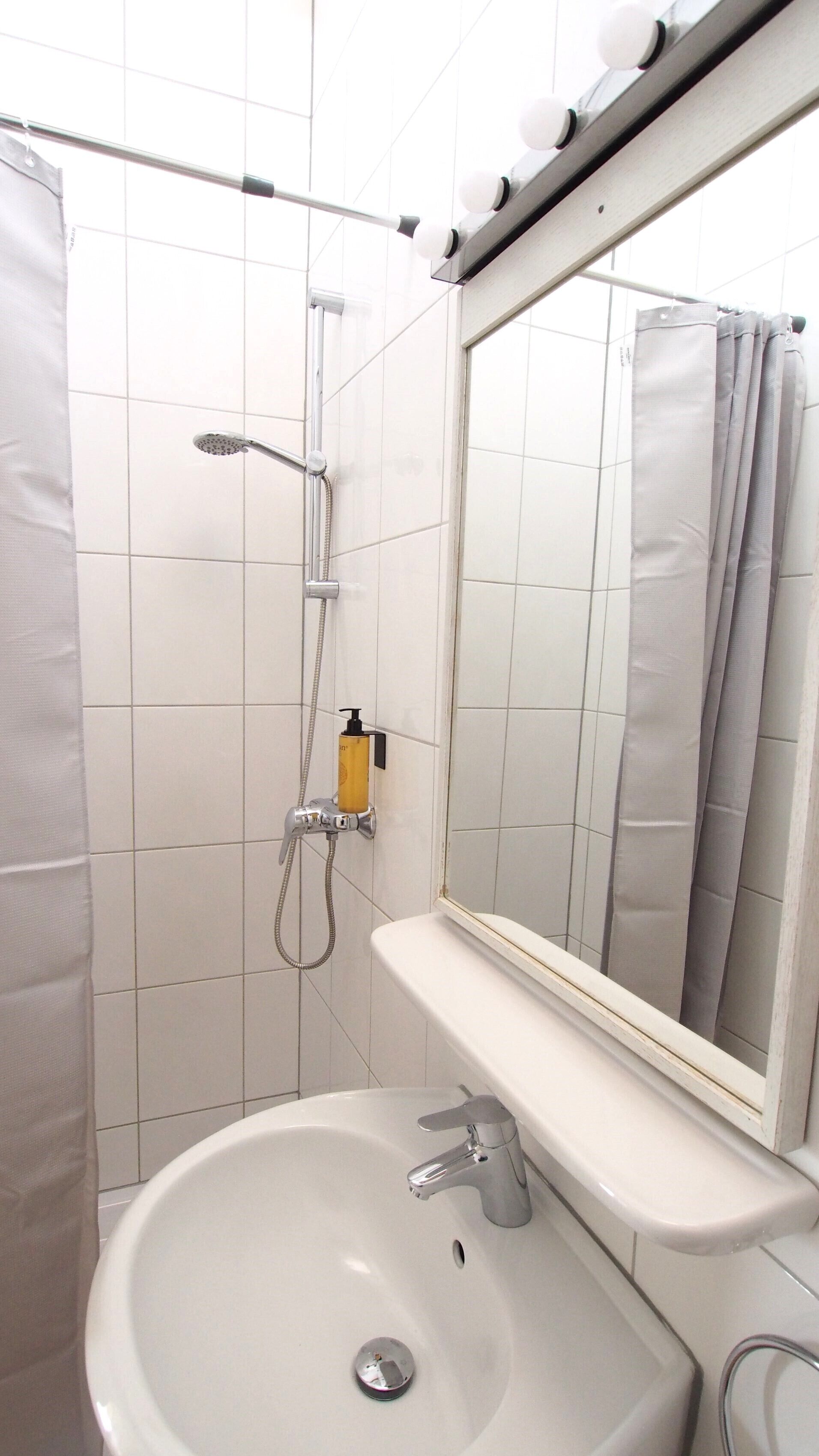 Ein Badezimmer mit einem weißen Waschbecken, einem Spiegel, einer Dusche inklusive Handbrause und einem Handtuchhalter.