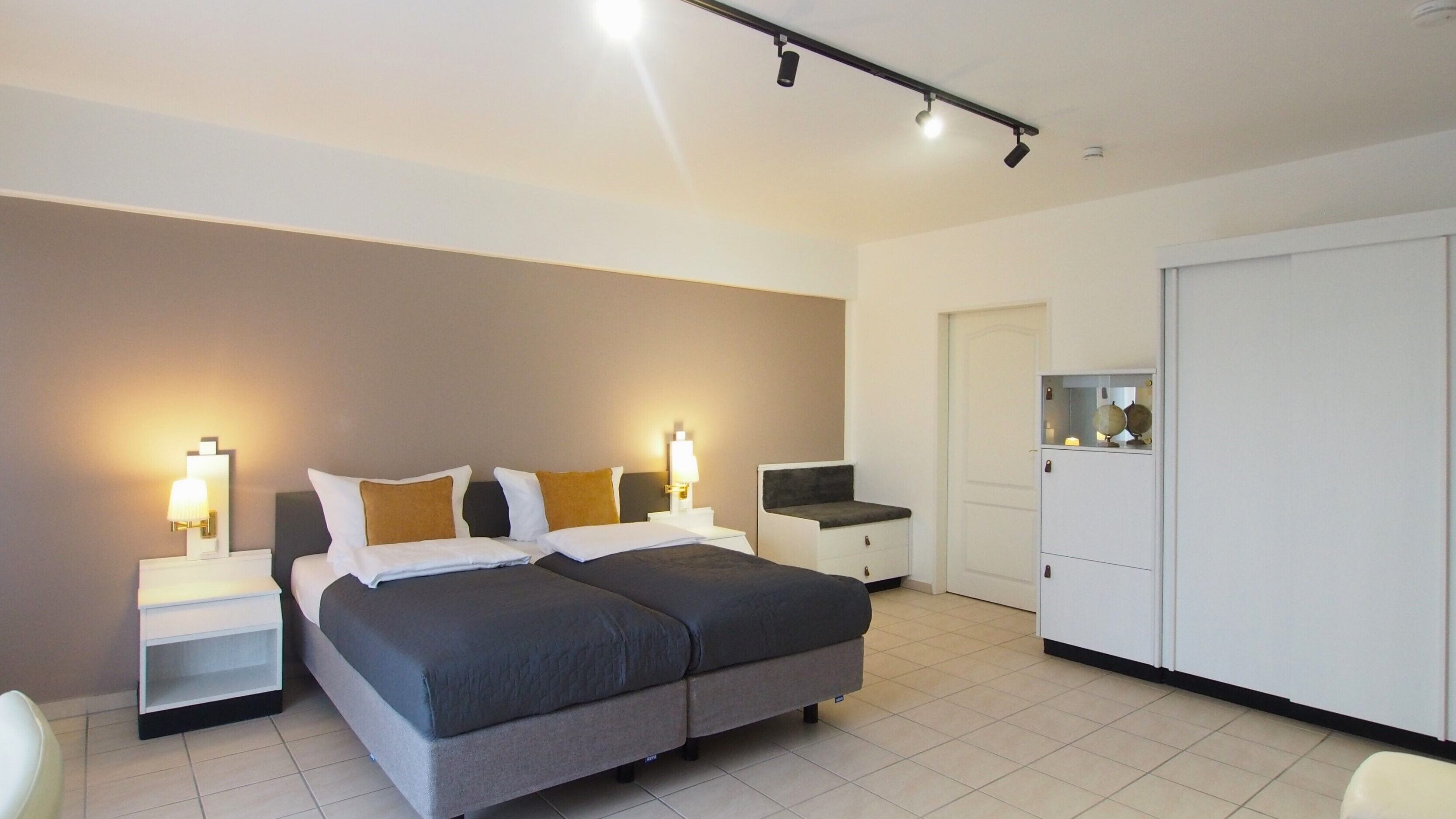 A modern hotel room with a large bed, bedside tables, a desk, and a wardrobe.