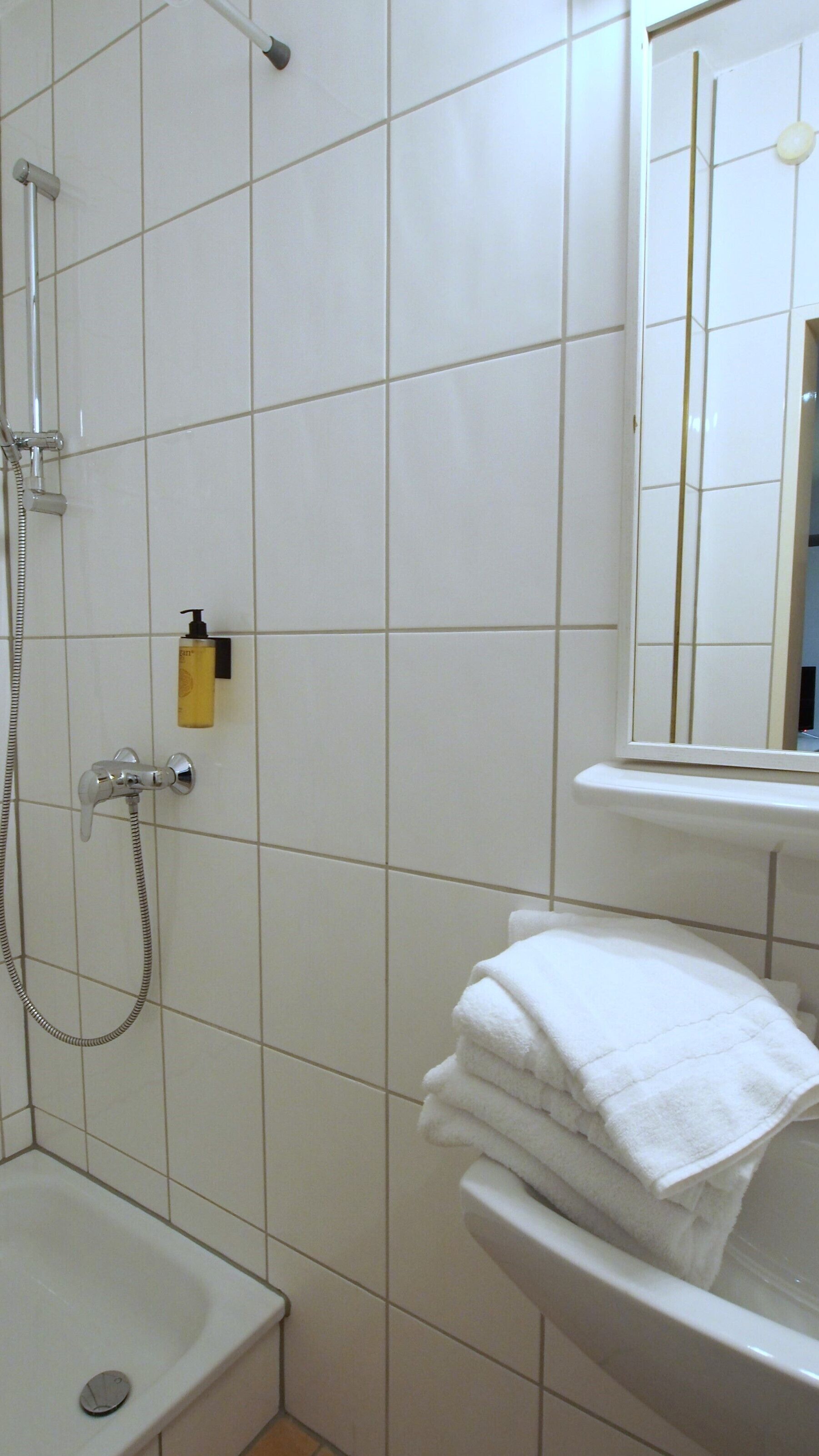 Un bagno con piastrelle bianche, una doccia, un lavandino e uno specchio.