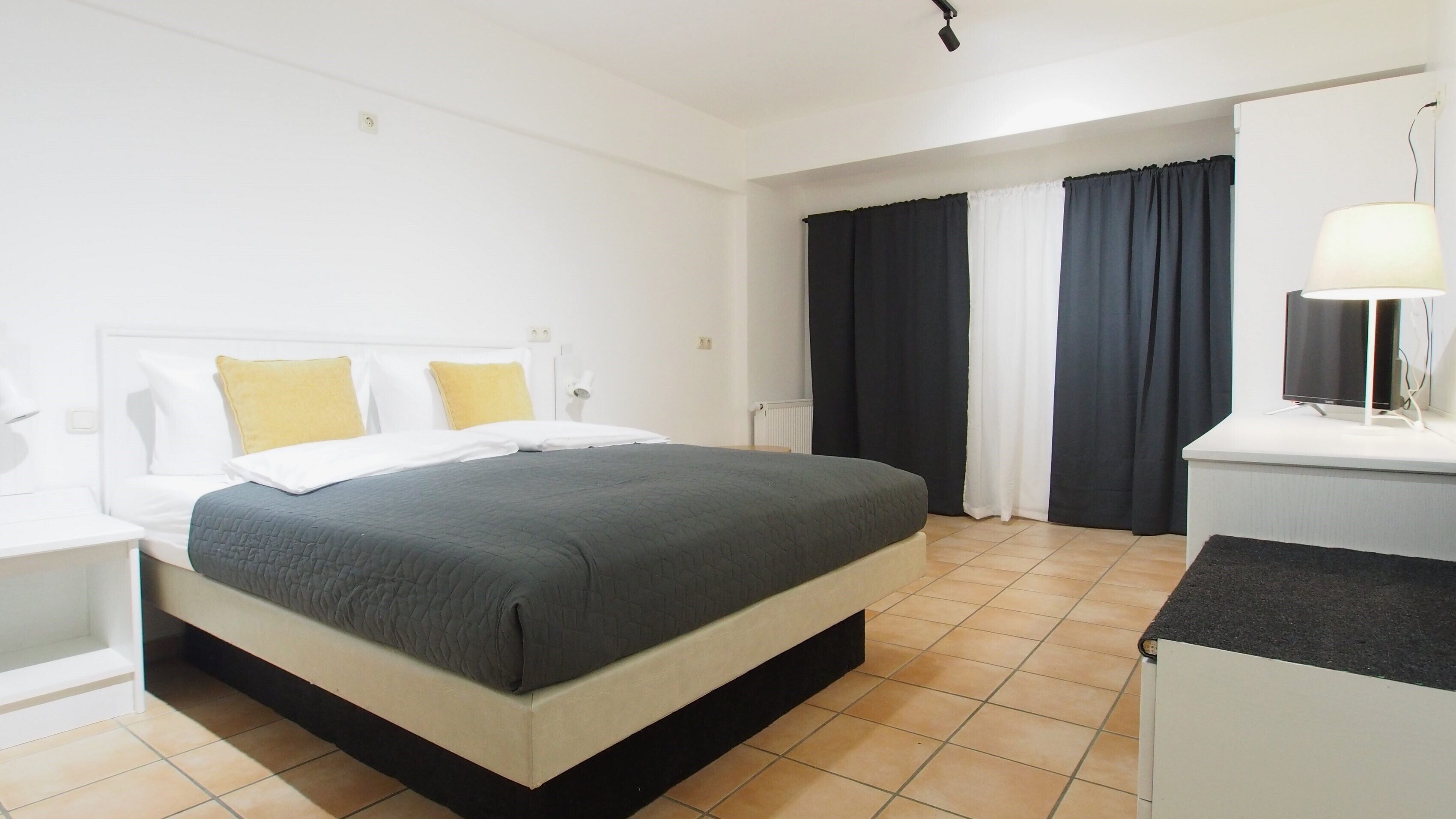 A hotel room with a bed, a bedside table, a lamp, and a window with curtains.