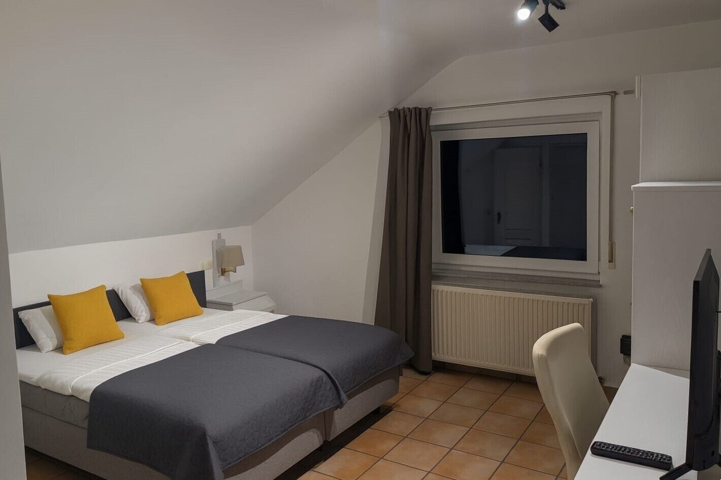 Una habitación pequeña y bien iluminada, con cama, escritorio y ventana.