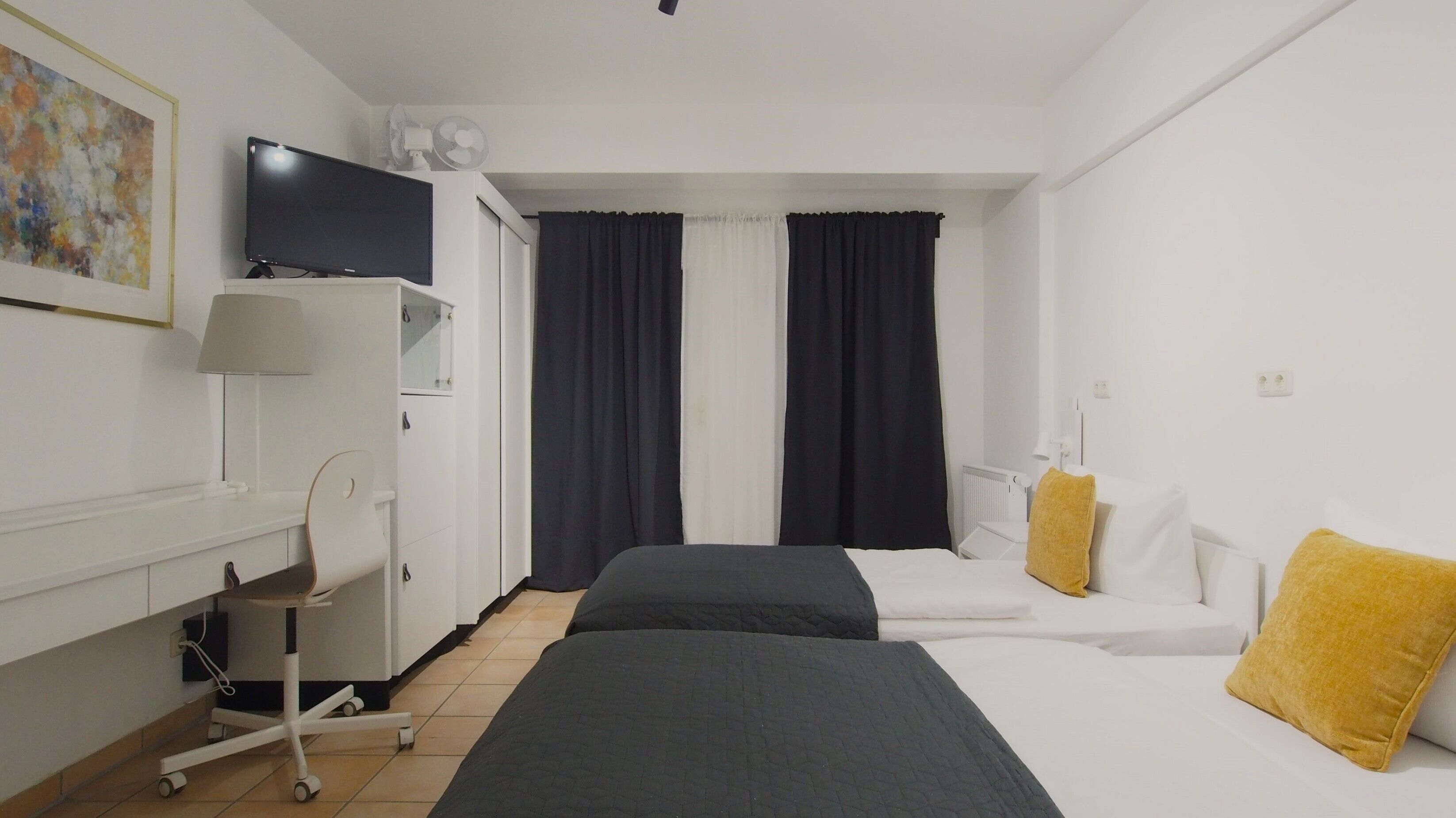 Une chambre d’hôtel avec deux lits, un bureau, une chaise, une télévision et un radiateur.