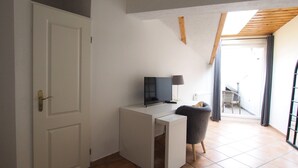 Una habitación pequeña y moderna con un escritorio blanco, una silla, un televisor y una ventana con vistas al exterior.