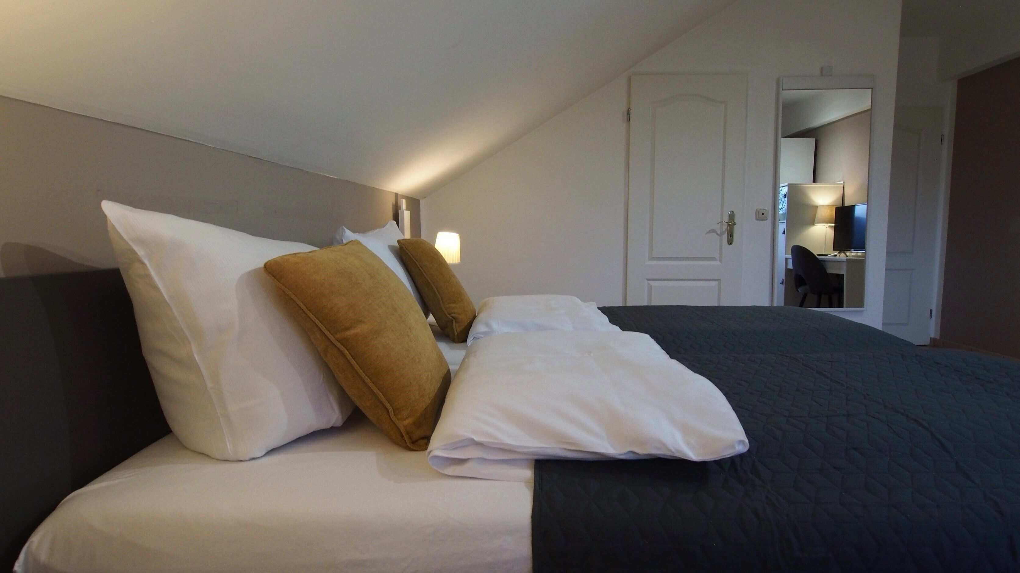 Een hotelkamer met een netjes opgemaakt bed, een deur en een klein bureau met een stoel.