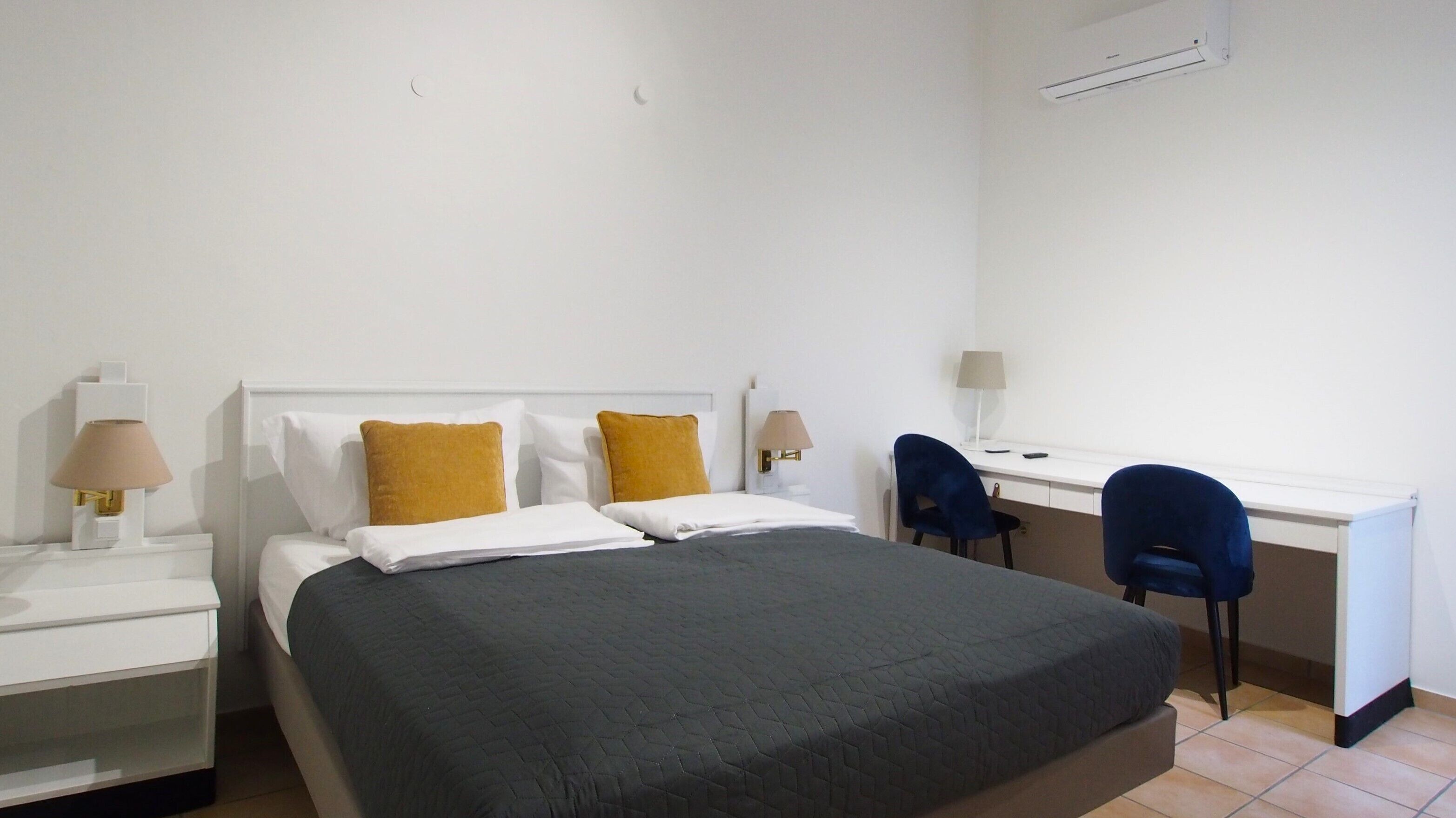 Een hotelkamer met een bed, twee stoelen, een bureau en een spiegel.