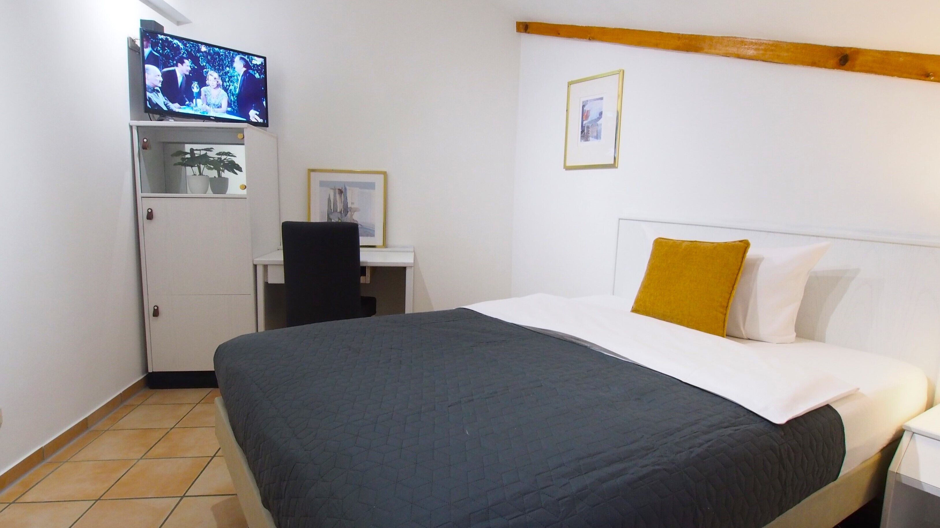 A bedroom with a bed, a desk, a television, and a small cabinet.