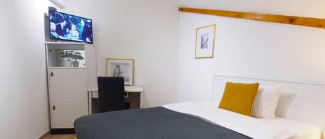 A bedroom with a bed, a desk, a television, and a small cabinet.