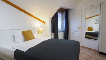 A hotel room with a bed, a nightstand with a lamp, a window with curtains, and a door with a mirror.