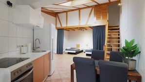 Cocina compacta con electrodomésticos modernos, comedor con mesa y sillas, y dormitorio tipo loft con cama y ventana.