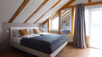 Une chambre avec un lit, des poutres en bois, une fenêtre et une vue sur un immeuble.