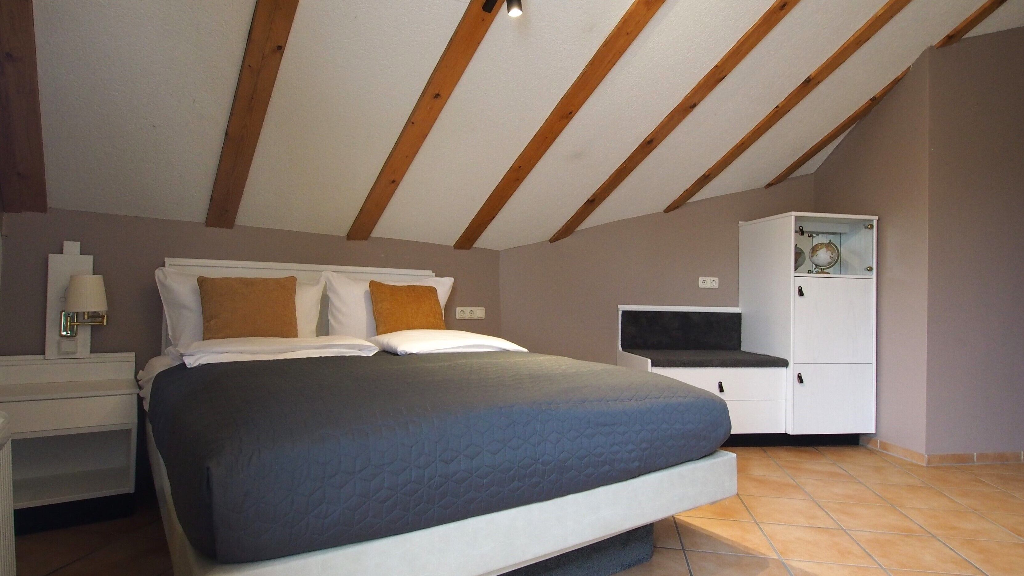 A bedroom with a bed, nightstands, a dresser, and a ceiling with wooden beams.