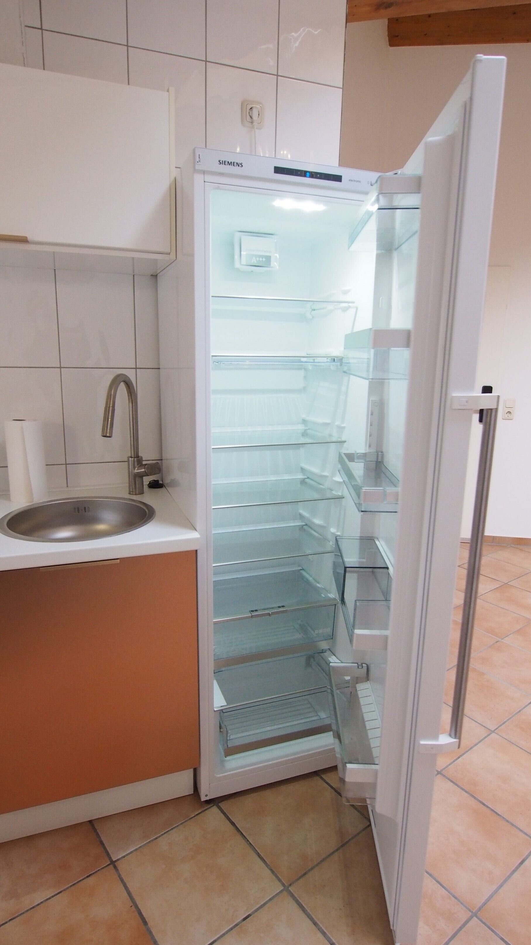 A kitchen with a Siemens refrigerator, a sink, and a tiled backsplash.