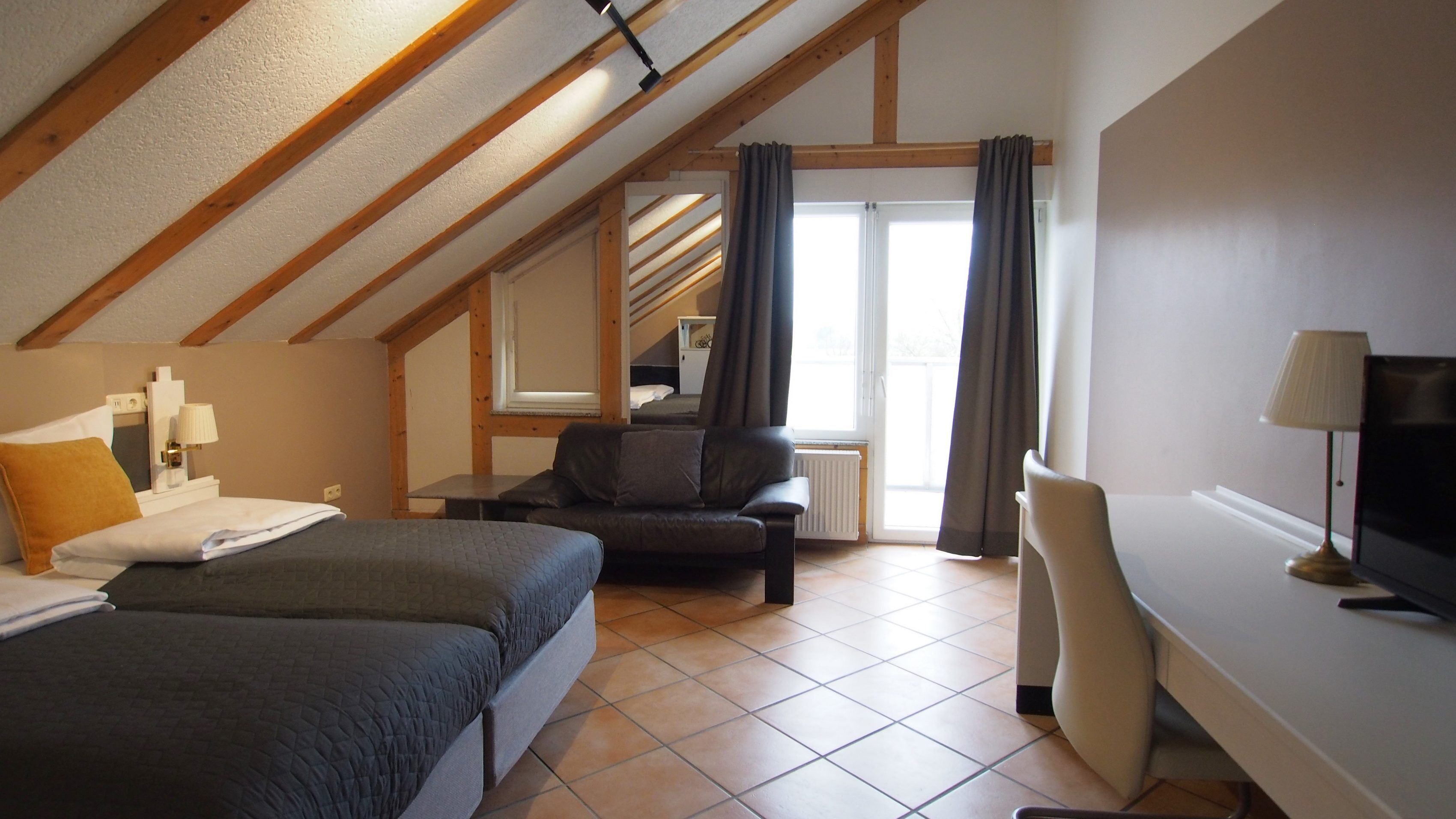 A hotel room with a loft-style ceiling, a bed, a desk, a chair, and a view of a balcony.
