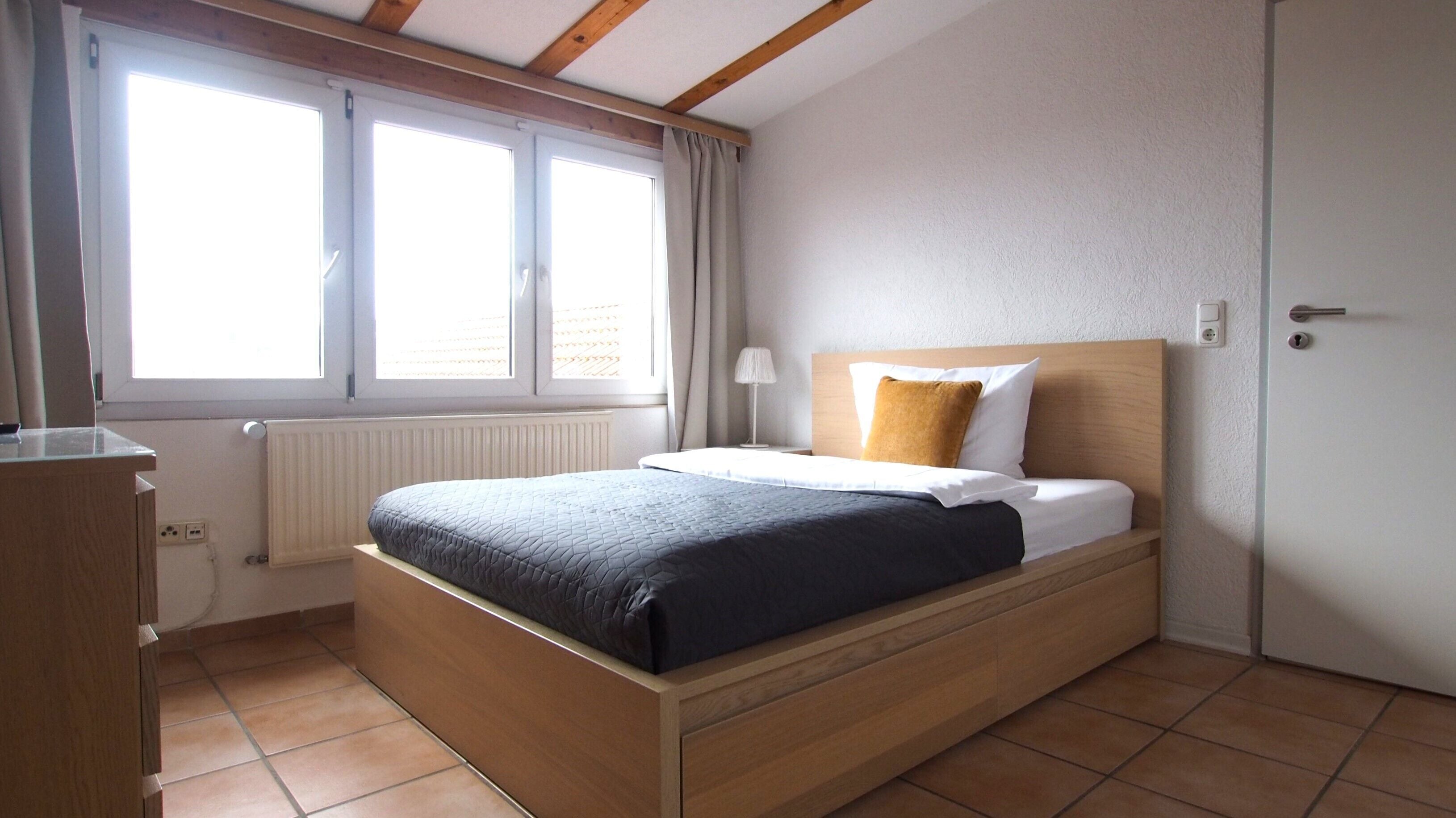 A bedroom with a wooden bed, a window with curtains, a bedside lamp, and a radiator.