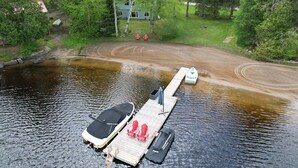 A dock with two boats, a covered area, and a house in the background.