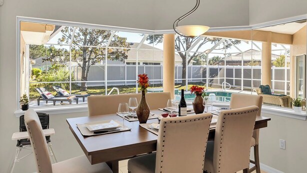 Un comedor con vista a un patio trasero y una piscina, que incluye una mesa para dos, sillas y una lámpara colgante.