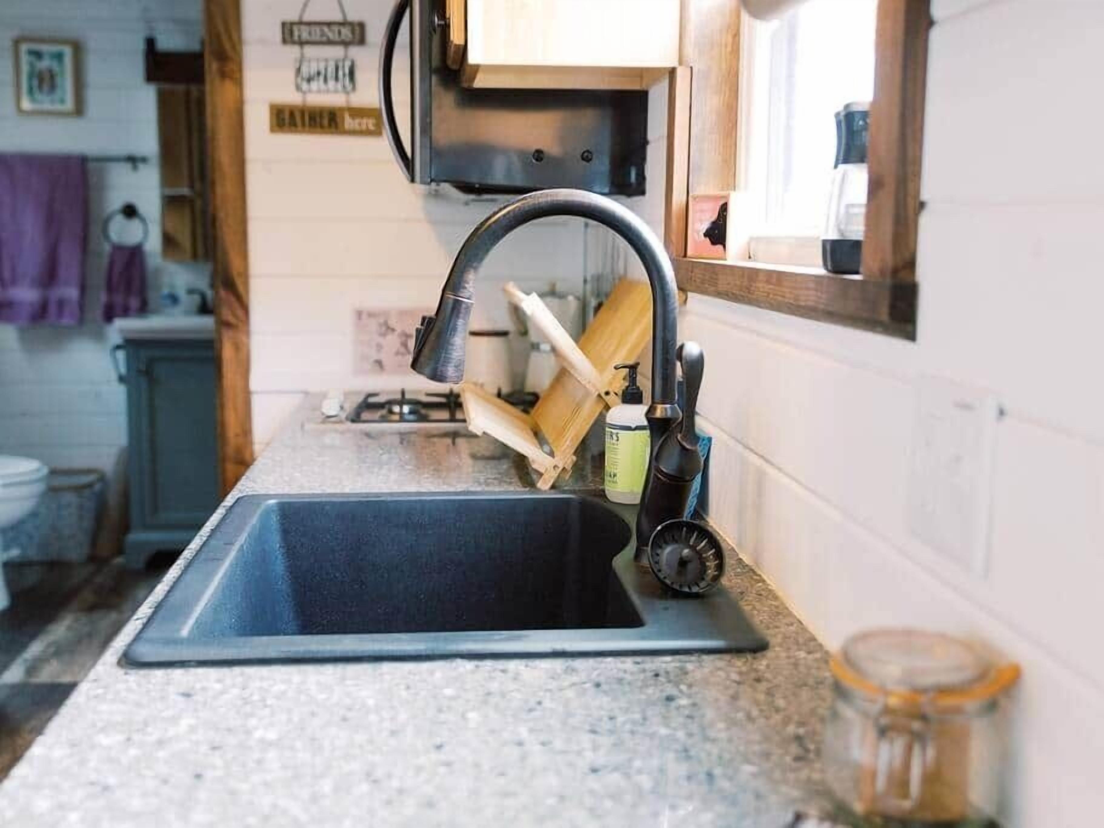 A kitchen with a sink, a faucet, a cutting board, and a jar on the counter.