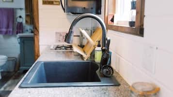 A kitchen with a sink, a faucet, a cutting board, and a jar on the counter.