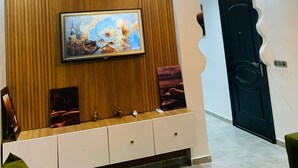 Ein modernes Wohnzimmer mit einer Wandpaneele aus Holz, einem Flachbildfernseher, einer weißen Unterhaltungsanlage und einer markanten schwarzen Tür.