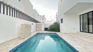 Ein moderner Poolbereich mit einem klaren blauen Pool, weißen Wänden und einer Wand als Steinakzent.