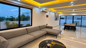 Ein modernes Wohnzimmer mit einem Ecksofa, einem runden Couchtisch und einem Essbereich mit Tisch und Stühlen.