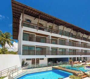 A multi-story hotel with balconies, a swimming pool, and a clear blue sky. - Porto Beach Residence (Ipojuca)