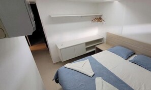 A bedroom with a bed, a bedside table, a wardrobe, and a hanging rack. - Porto Beach Residence (Ipojuca)
