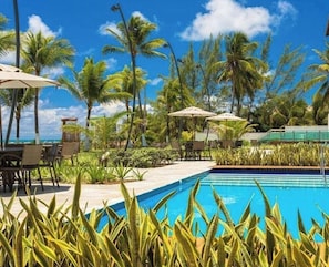 A pool area with palm trees, umbrellas, and lounge chairs. - Porto Beach Residence (Ipojuca)