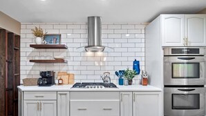 A modern kitchen with white cabinets, a stainless steel range hood, and built-in ovens. - Lake Escape-Pool Table-Kids Game Room-Wii-Foosball (Avon Lake)