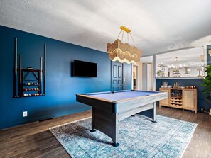 Une table de billard dans une pièce aux murs bleus, avec un plancher en bois et un tapis à motifs.
