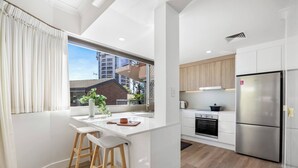 A modern kitchen with white cabinetry, a stainless steel refrigerator, and a large window overlooking a residential area. - Sunlit Durham Walk to Glenelg Beach Dining and Bars (Glenelg)