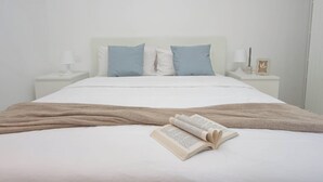 Un lit bien fait, avec un livre et une couverture, des murs blancs et des tables de chevet avec des lampes.